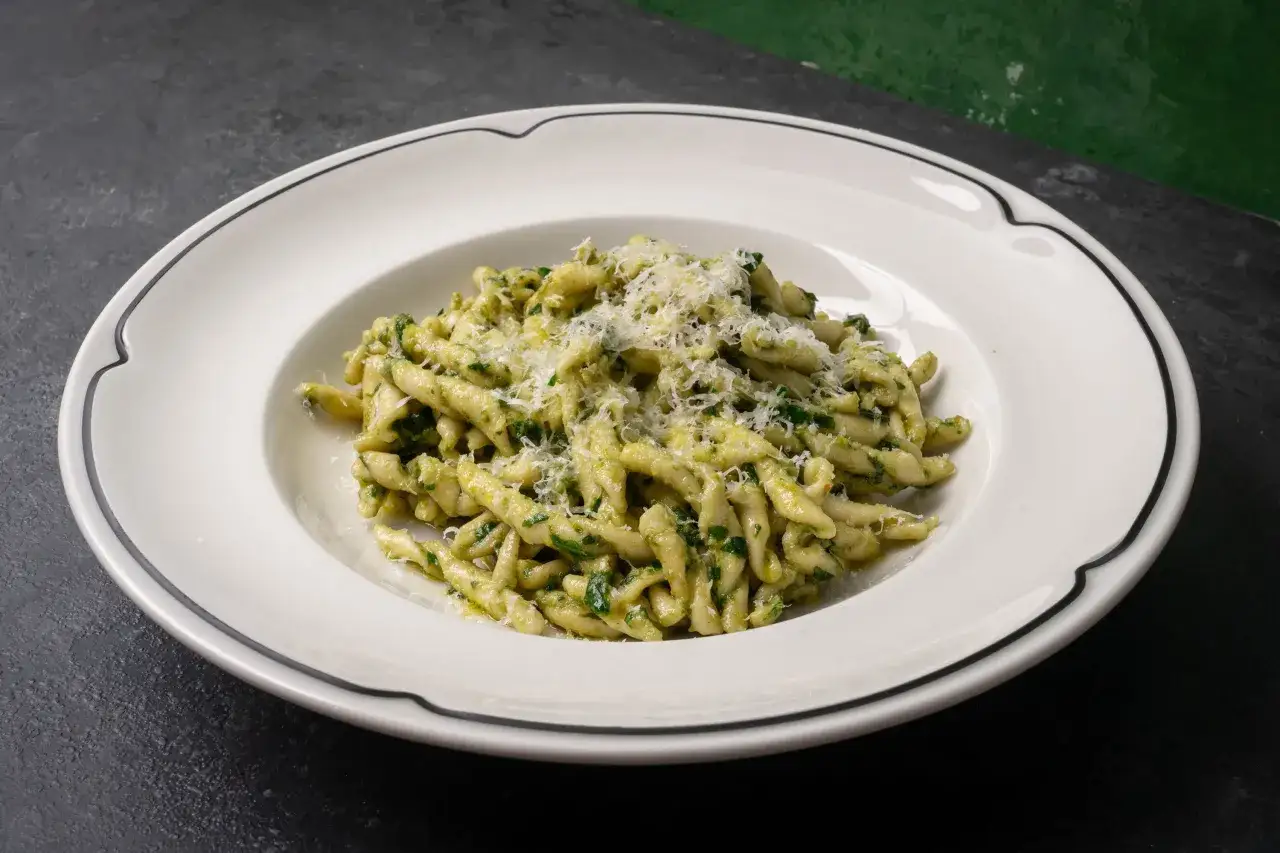 Un plato de pasta al pesto, con queso rallado espolvoreado, listo para disfrutar.