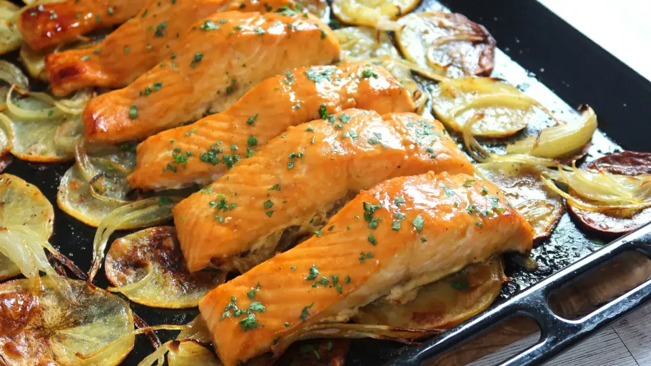 Filetes de salmón al horno, dorados y jugosos, reposan sobre patatas y cebolla asadas. Un plato delicioso y saludable.