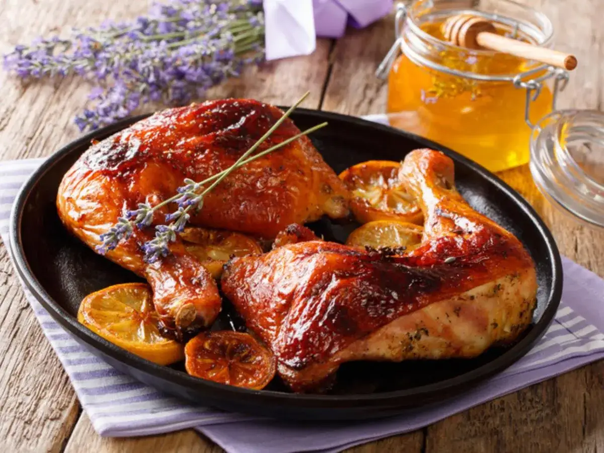 Muslos de pollo al horno dorados y jugosos, servidos con rodajas de lim&oacute;n y un toque de lavanda. Un tarro de miel dorada acompa&ntilde;a este delicioso plato.