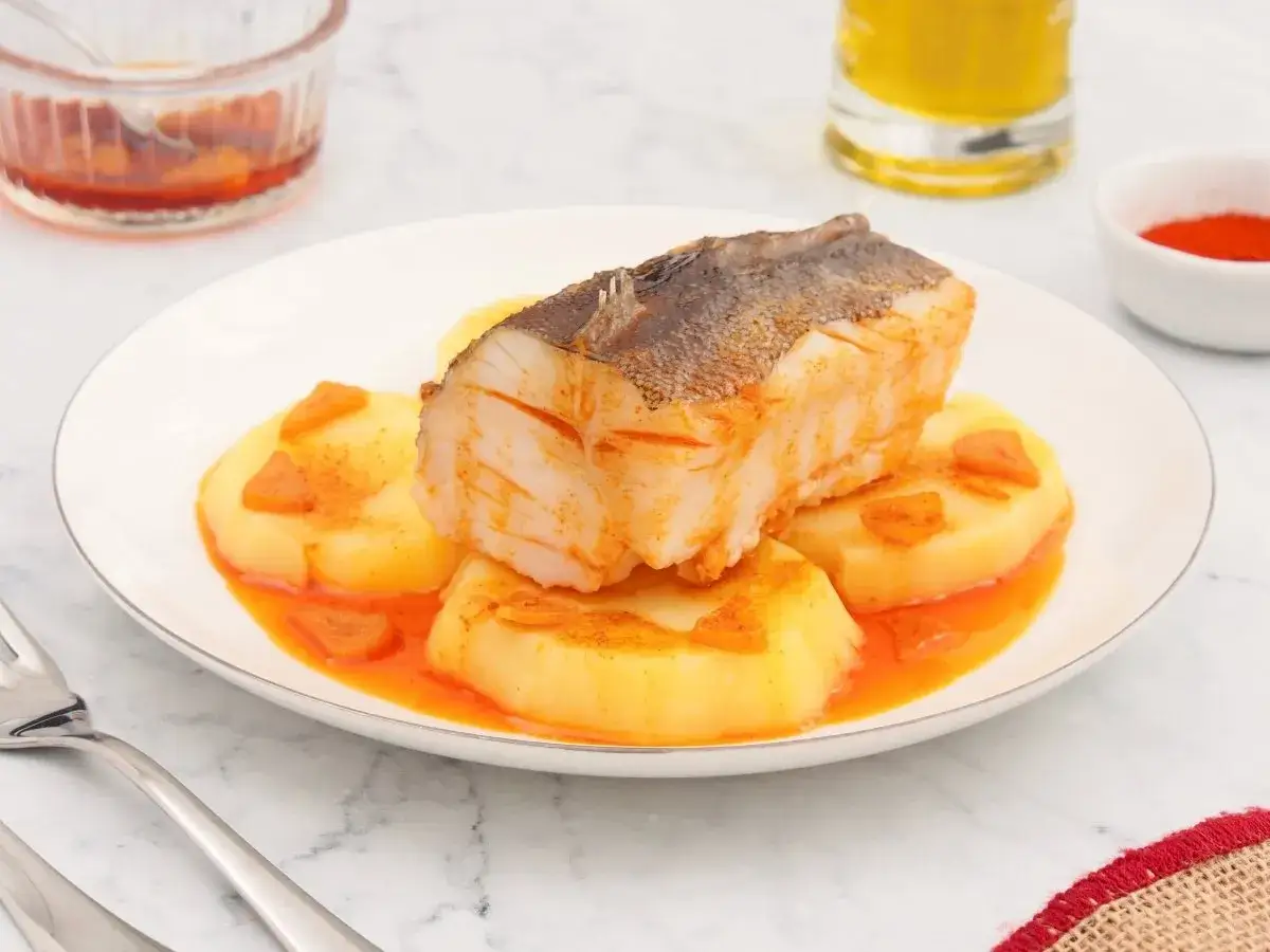 Un delicioso bacalao a la gallega, con patatas y pimentón, servido en un plato blanco.