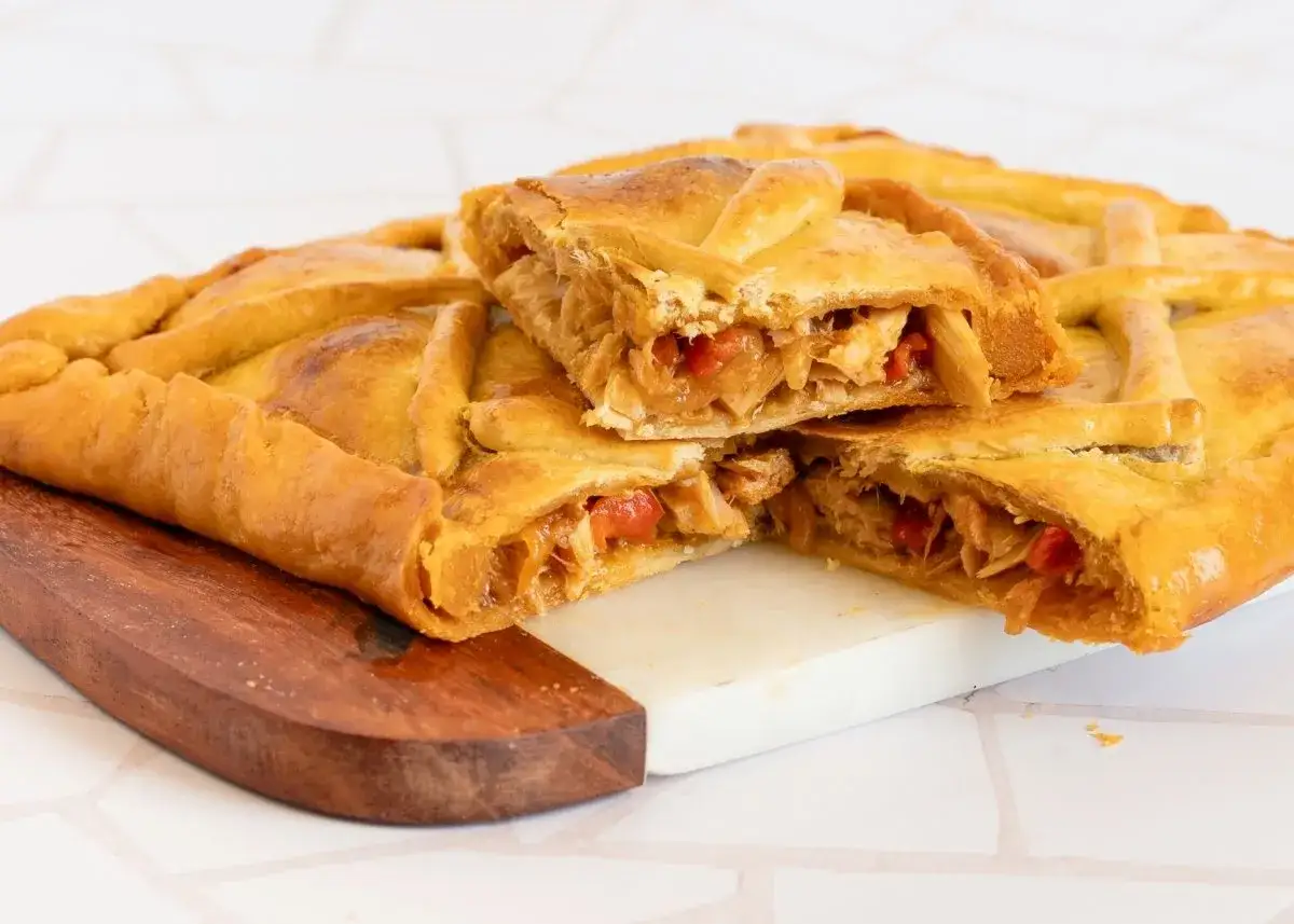 Empanada gallega dorada y crujiente, cortada para mostrar su relleno de at&uacute;n y pimientos.