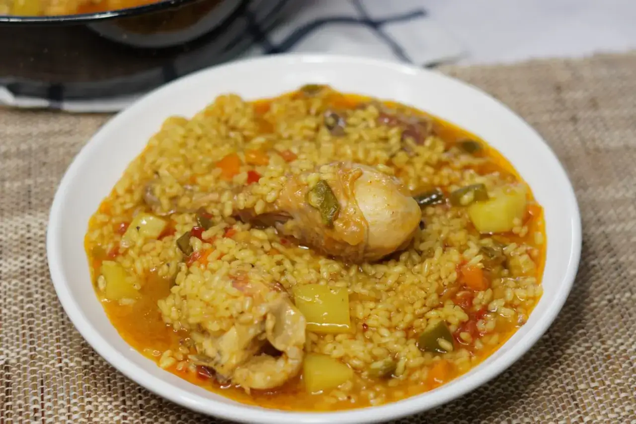 Un plato de arroz con pollo, jugoso y lleno de verduras como pimientos y patatas.