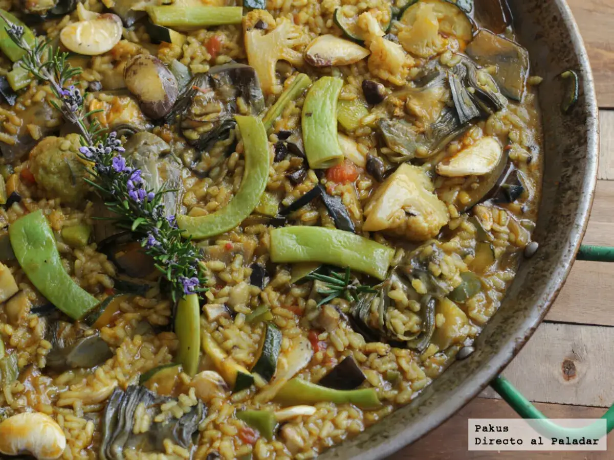 Paella de verduras recién hecha, con alcachofas, calabacín, pimientos y romero. Un plato lleno de sabor y color.