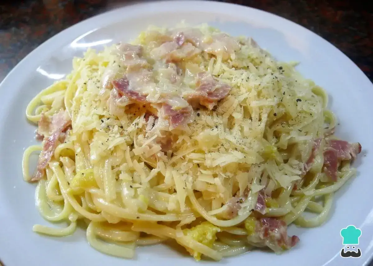 Un plato de pasta carbonara cremoso, cubierto con queso rallado y trozos de tocino crujiente.