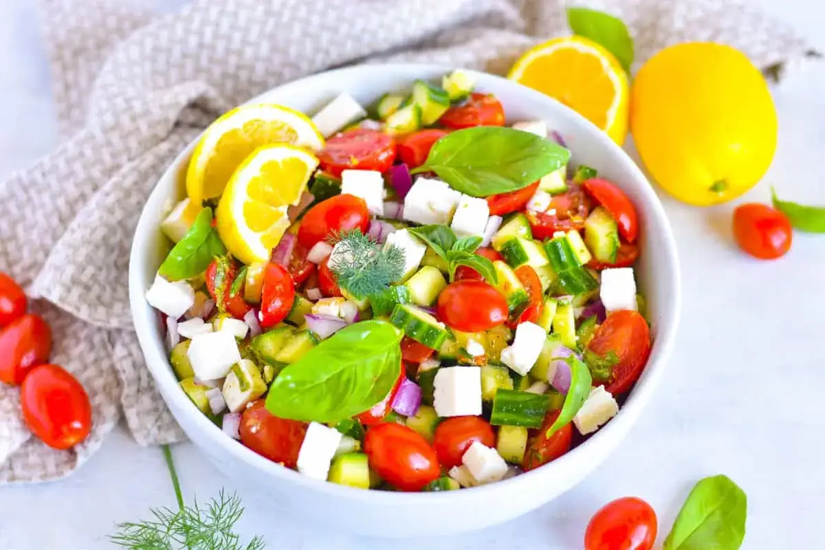 Ensalada de pepino fresca con tomates cherry, queso feta, cebolla morada y hojas de albahaca, aderezada con limón.