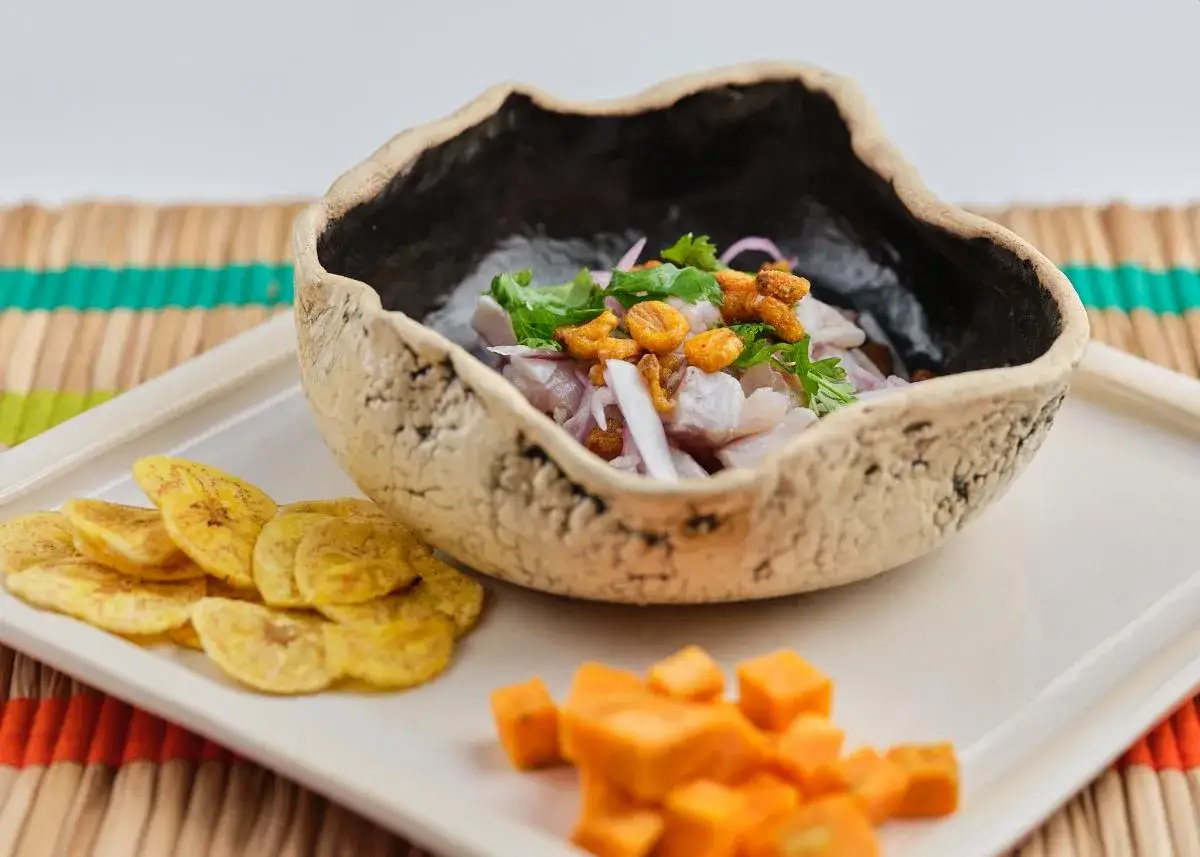 Delicioso ceviche de corvina fresco, servido en un cuenco r&uacute;stico, acompa&ntilde;ado de pl&aacute;tano frito y cubos de camote.