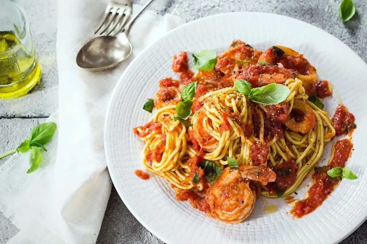 Espaguetis con gambas, un plato vibrante con pasta dorada, gambas jugosas y salsa de tomate casera, adornado con hojas de albahaca fresca.