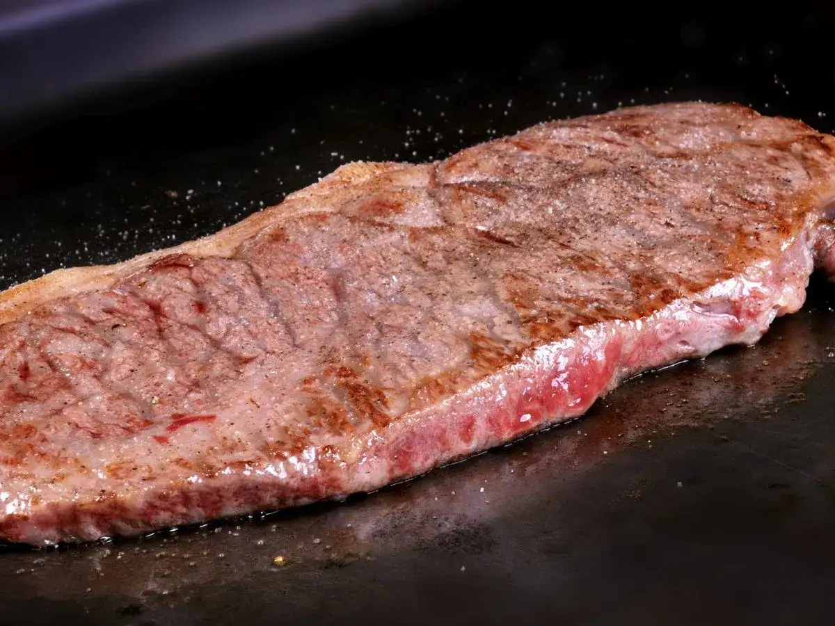 Un jugoso filete de ternera se cocina a la perfecci&oacute;n en una plancha caliente, con sal y pimienta esparcidas.