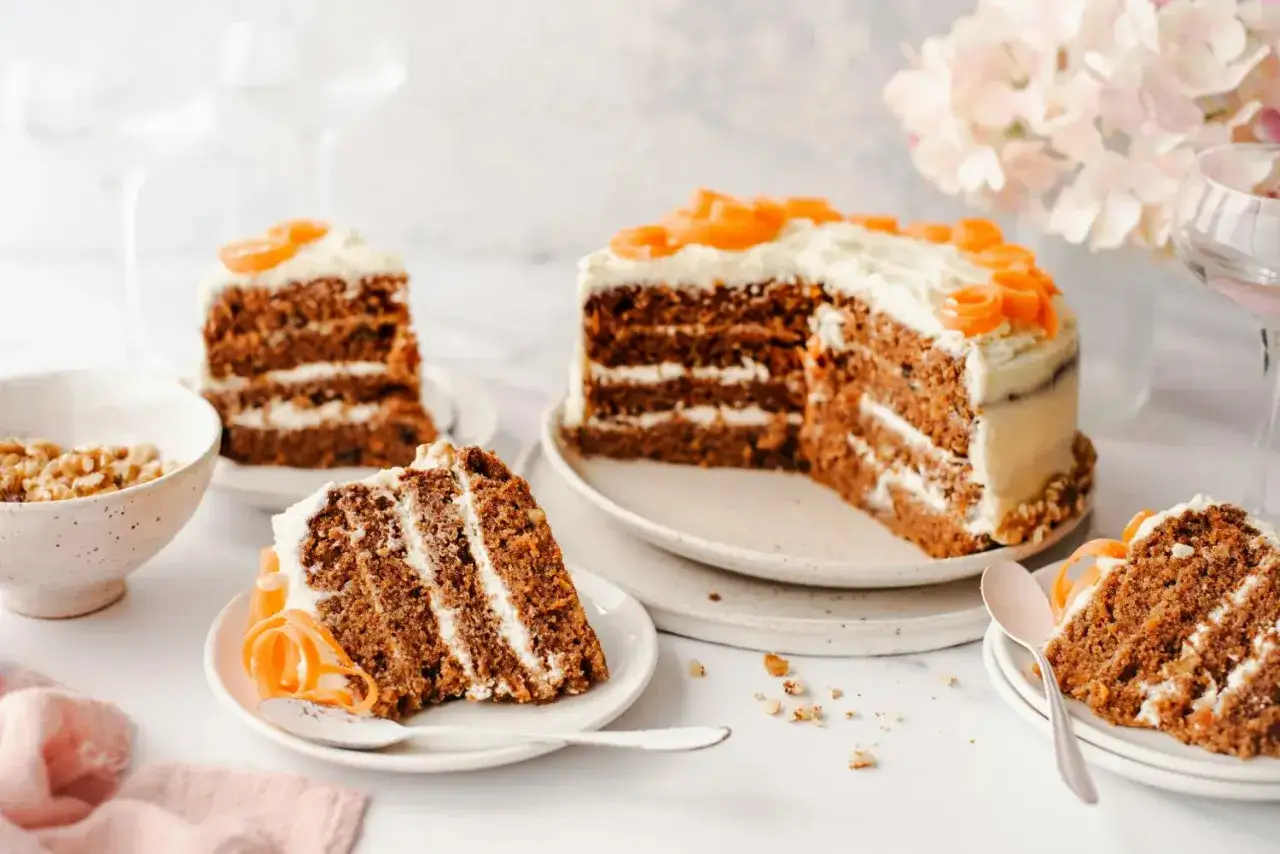 Delicioso pastel de zanahoria con glaseado cremoso y decoraciones de zanahoria. Se ven varias rebanadas y nueces.