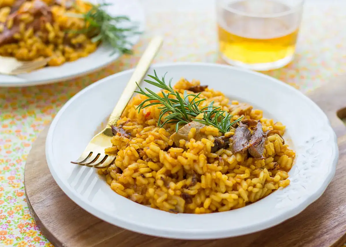Delicioso arroz con secreto ibérico y setas, adornado con romero fresco. Un plato reconfortante y lleno de sabor.