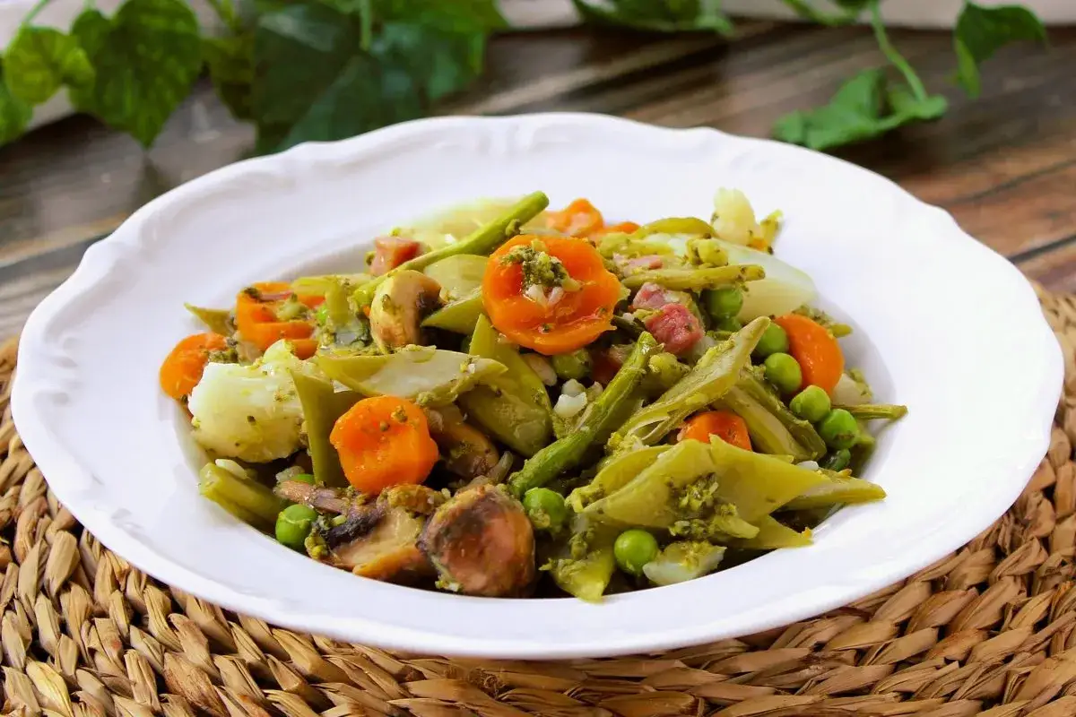 Un plato de menestra de verduras con judías verdes, zanahoria, guisantes, patatas y champiñones, todo ello aderezado con una salsa verde.