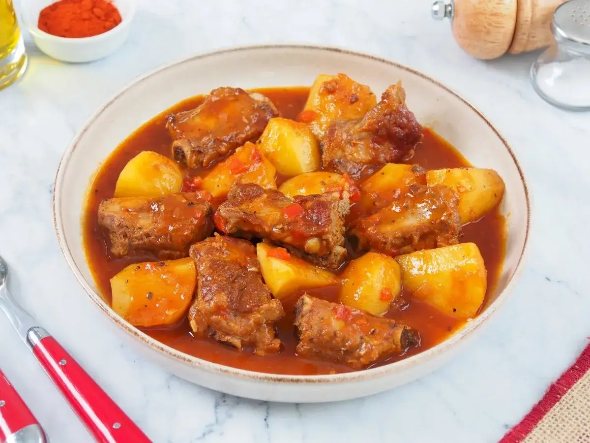 Un plato humeante de patatas con costillas en una rica salsa roja.