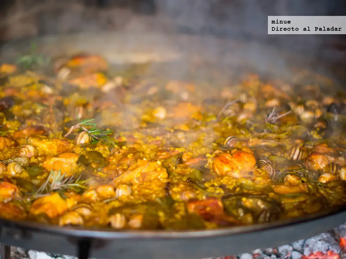 Paella valenciana con sus ingredientes: arroz, pollo, conejo, judías verdes y caracoles, cocinándose a fuego lento.