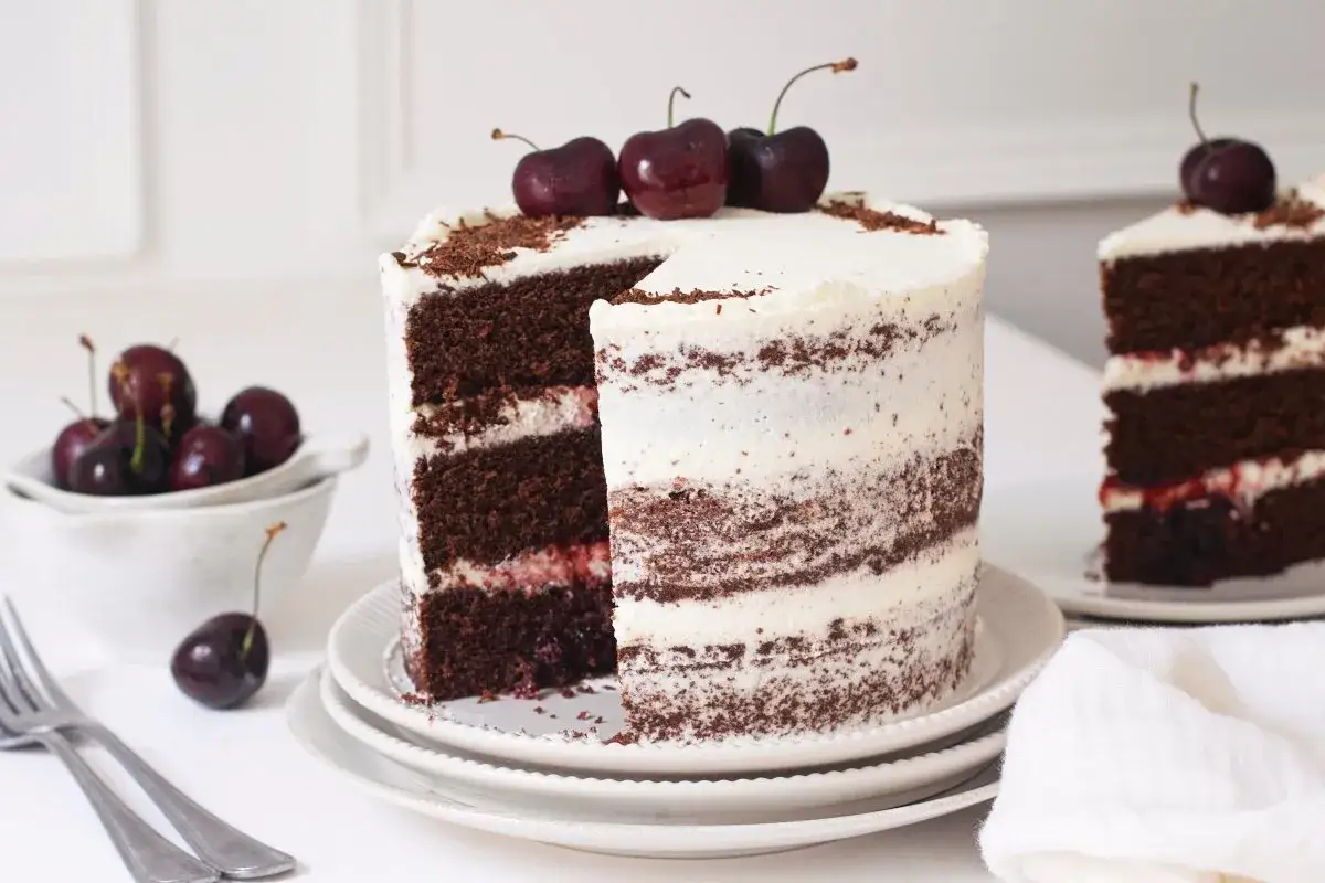 Tarta Selva Negra, con capas de bizcocho de chocolate, crema y cerezas, decorada con cerezas frescas y virutas de chocolate.