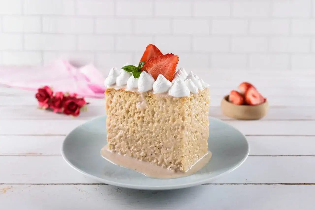 Delicioso trozo de tarta tres leches, cubierto con merengue, fresas y una hoja de menta. Un postre perfecto para cualquier ocasión.