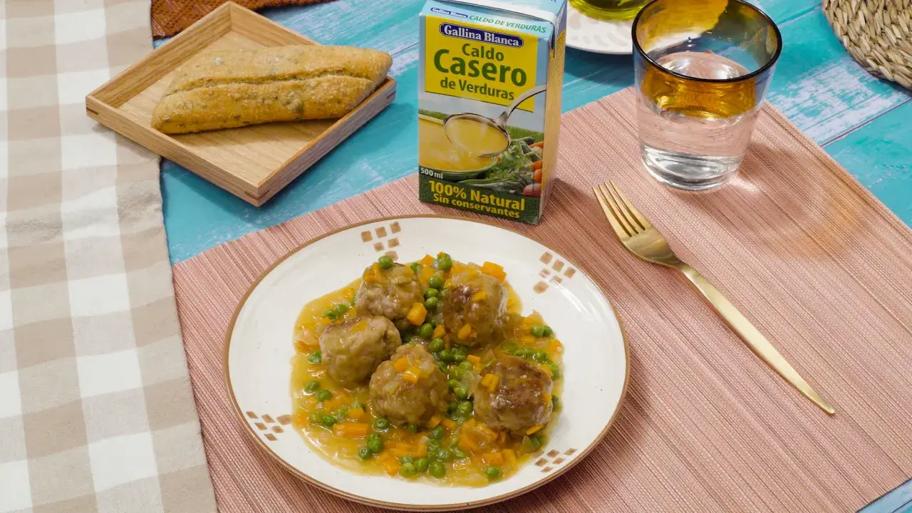 Albondigas a la jardinera con guisantes y zanahoria en salsa, acompañadas de pan y caldo de verduras.