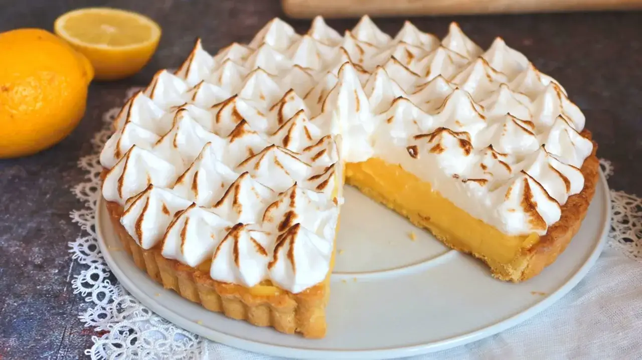 Un delicioso lemon pie con merengue dorado y una porci&oacute;n cortada, junto a limones frescos.