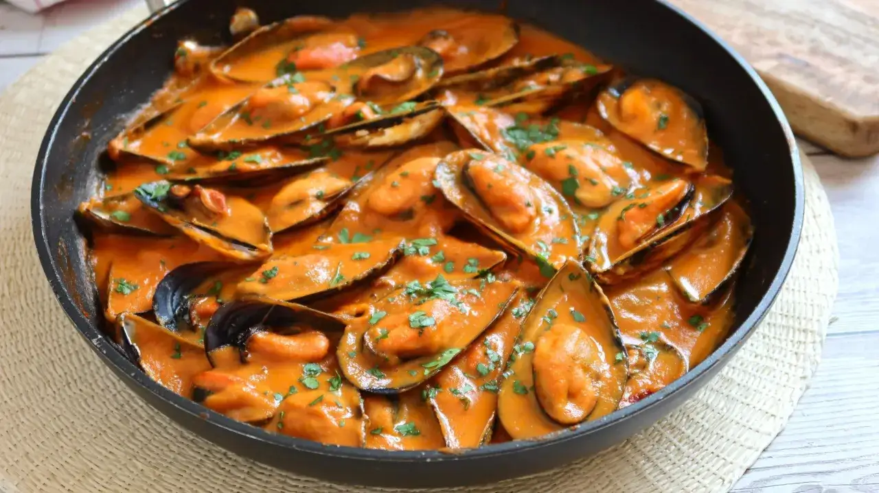 Mejillones con tomate en salsa cremosa, espolvoreados con perejil fresco. Un plato delicioso y fácil de preparar.