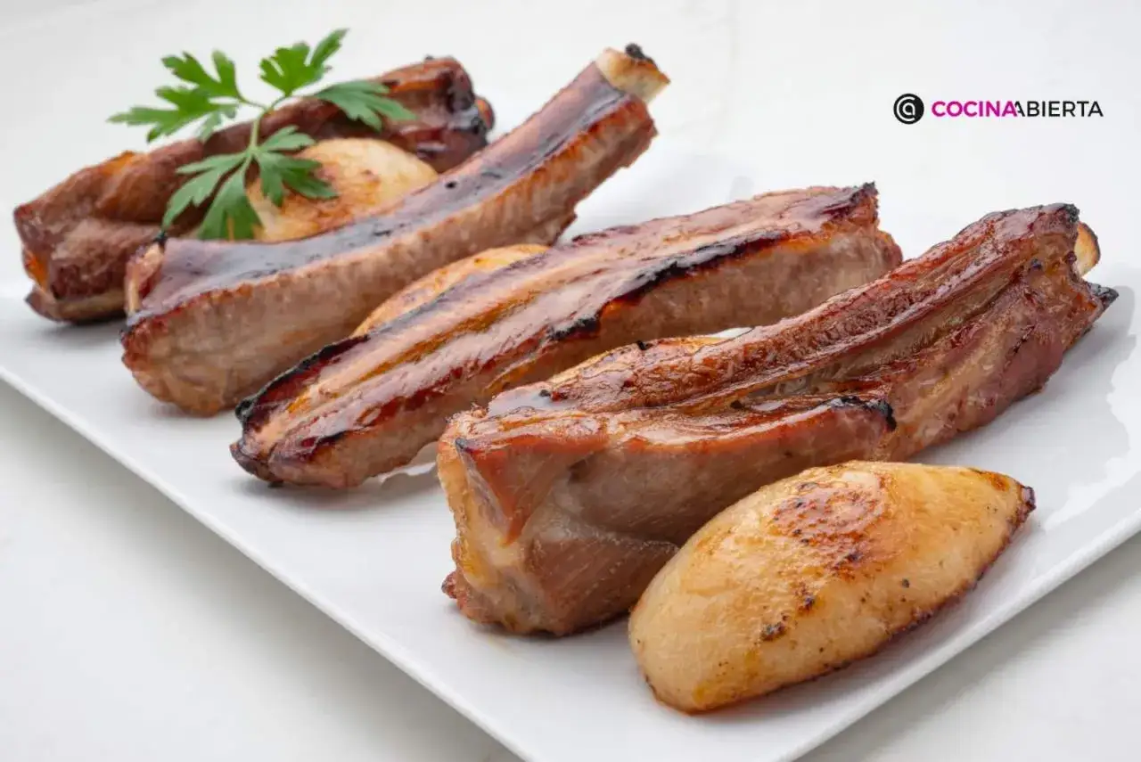 Costillas de cerdo jugosas y doradas, servidas en una bandeja blanca con una ramita de perejil.