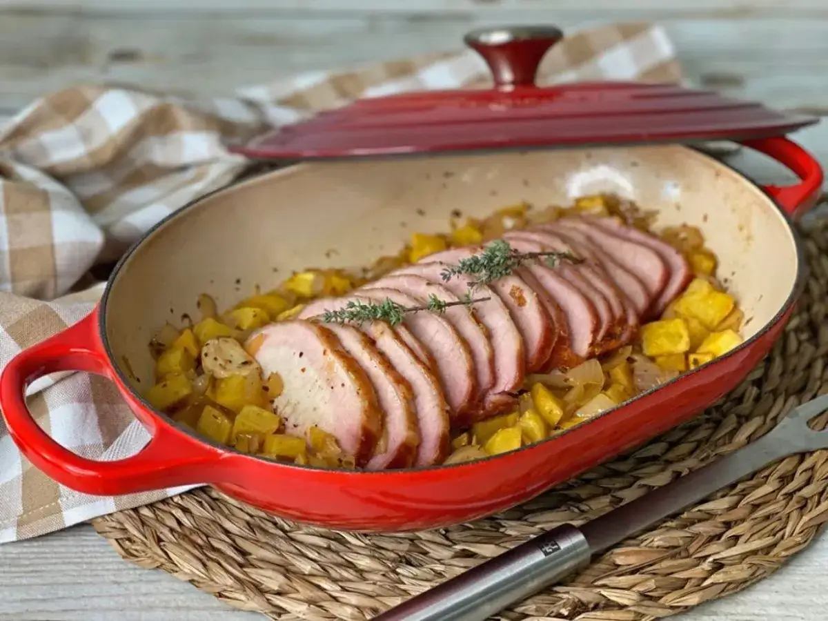 Lomo adobado jugoso y tierno, servido sobre patatas y cebolla doradas en una cazuela roja. ¡Un plato delicioso!