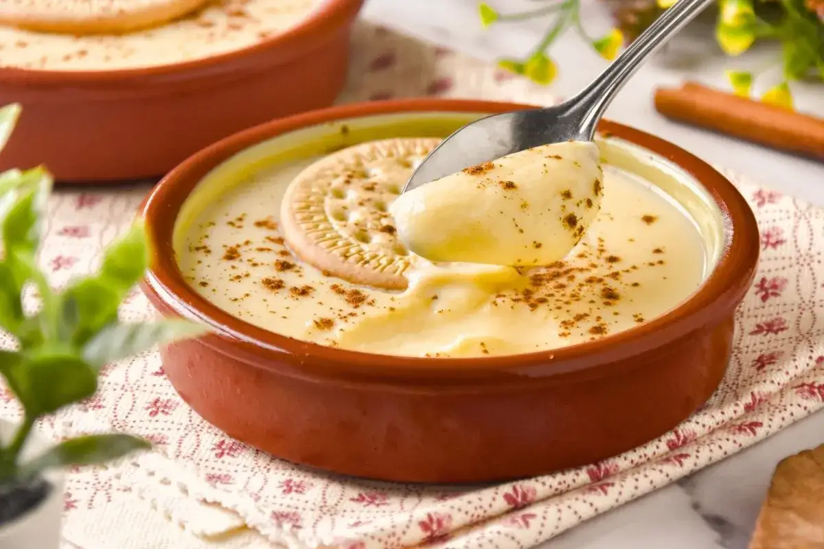 Cremosas natillas caseras, espolvoreadas con canela y coronadas con una galleta, listas para ser disfrutadas.
