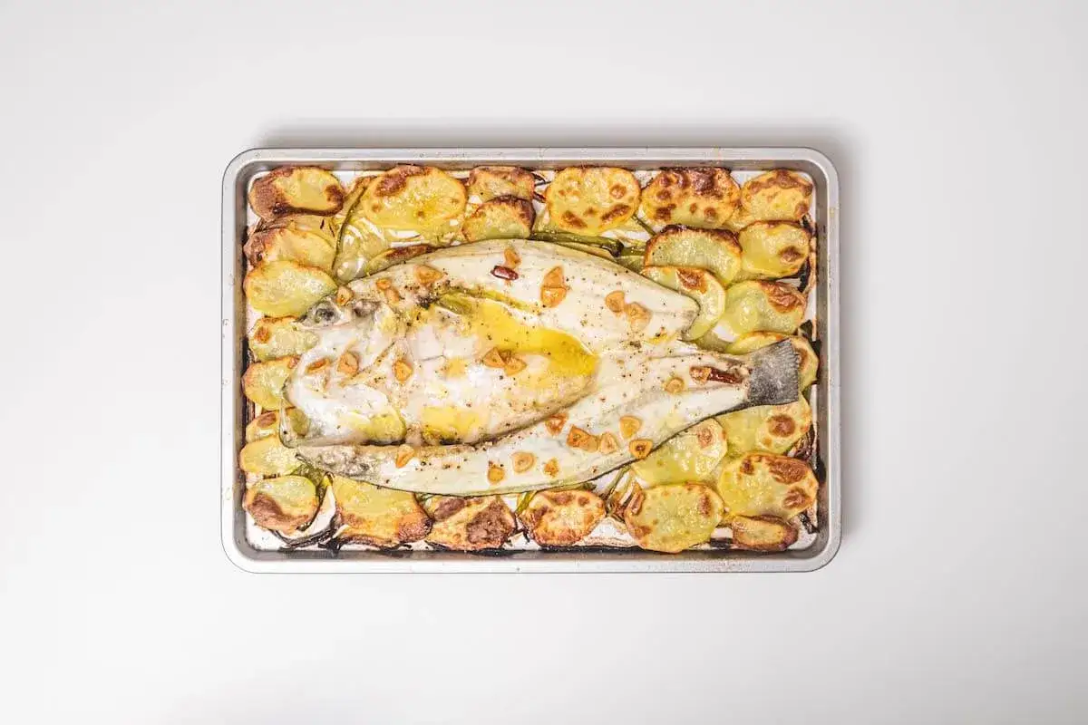 Lubina al horno con patatas y ajo, dorada y jugosa, lista para servir.