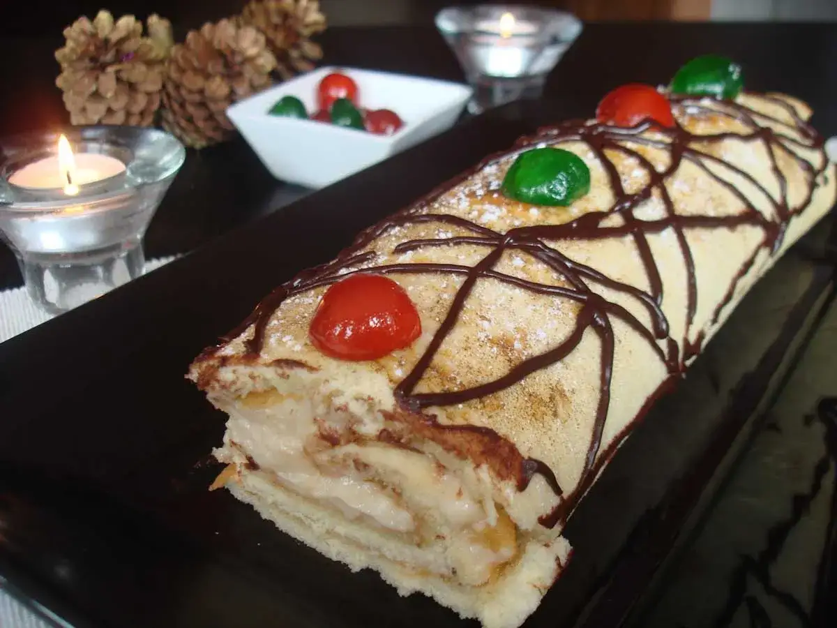 Un delicioso brazo de gitano con crema, decorado con chocolate y cerezas, listo para celebrar.