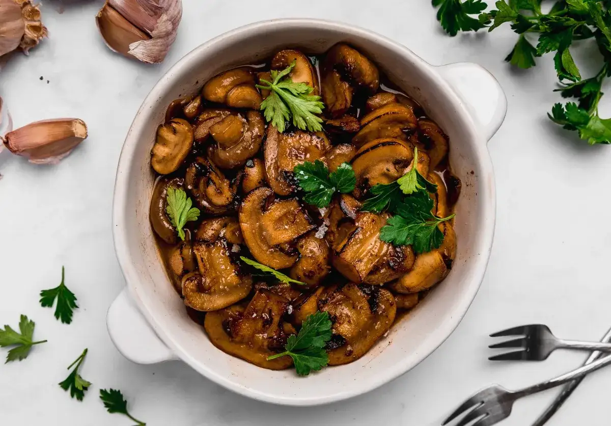 Deliciosos champiñones al ajillo, salteados con ajo y perejil fresco, servidos en un cuenco blanco.
