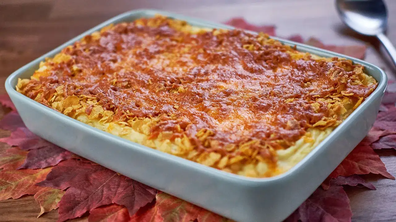 Pastel de patata gratinado con queso y cereales crujientes, servido sobre hojas de otoño.