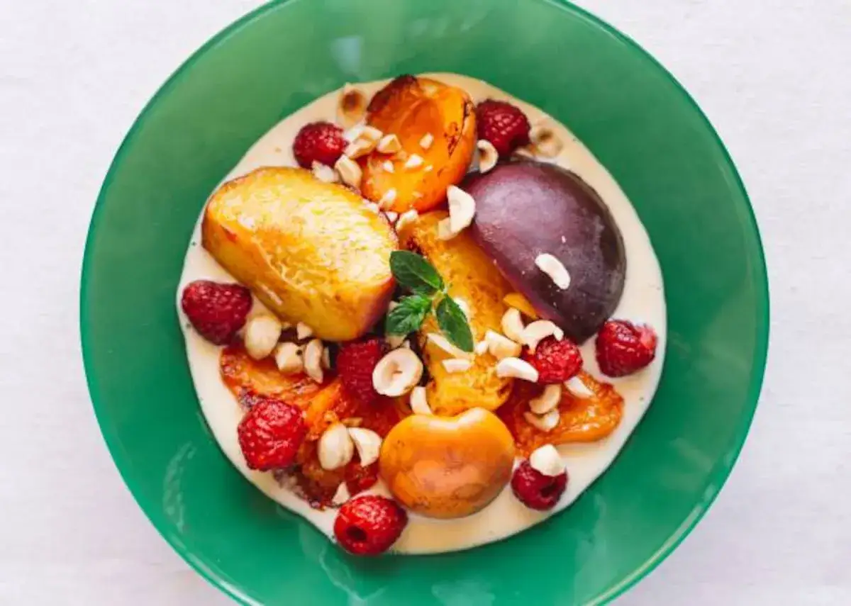 Frutas asadas con frambuesas, nueces y una generosa porción de crema inglesa en un plato verde.