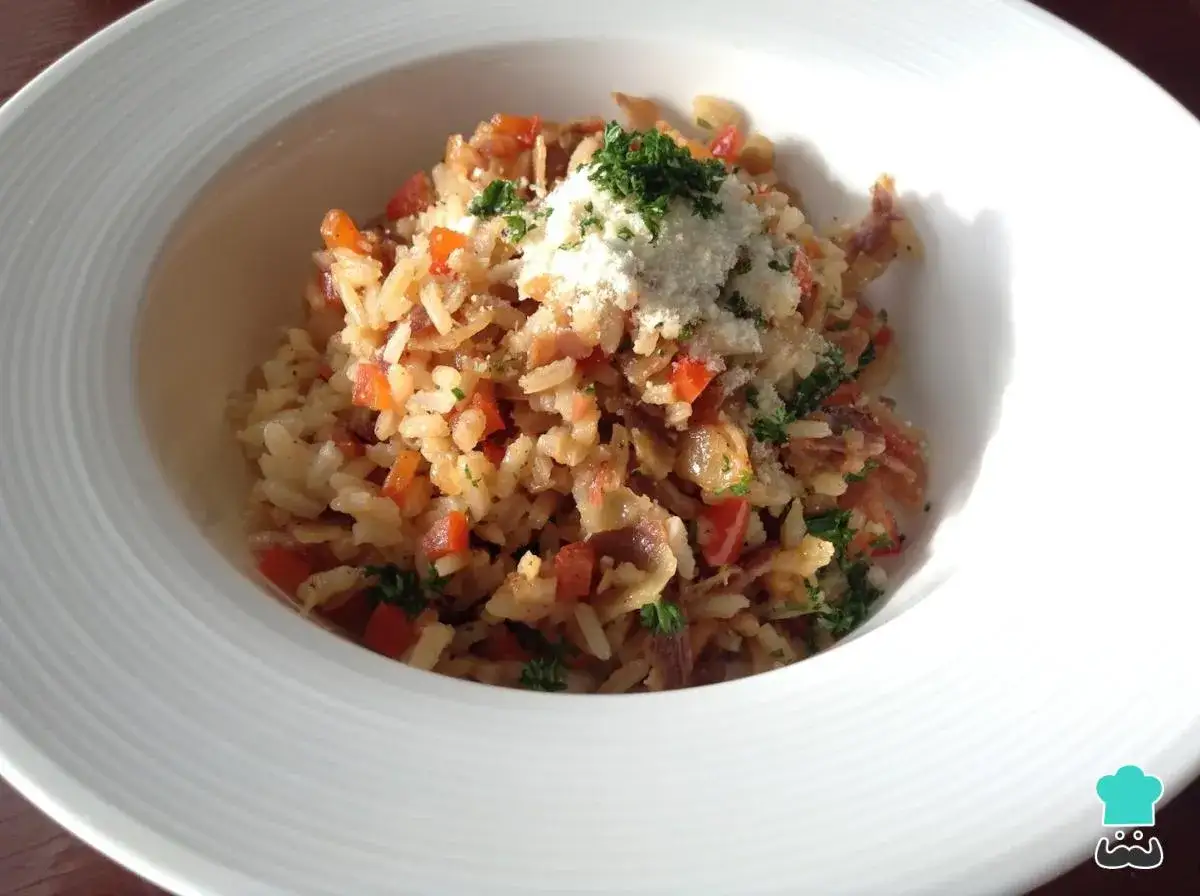 Delicioso arroz a la milanesa con trozos de pimiento rojo y tocino crujiente, coronado con queso rallado y perejil fresco.