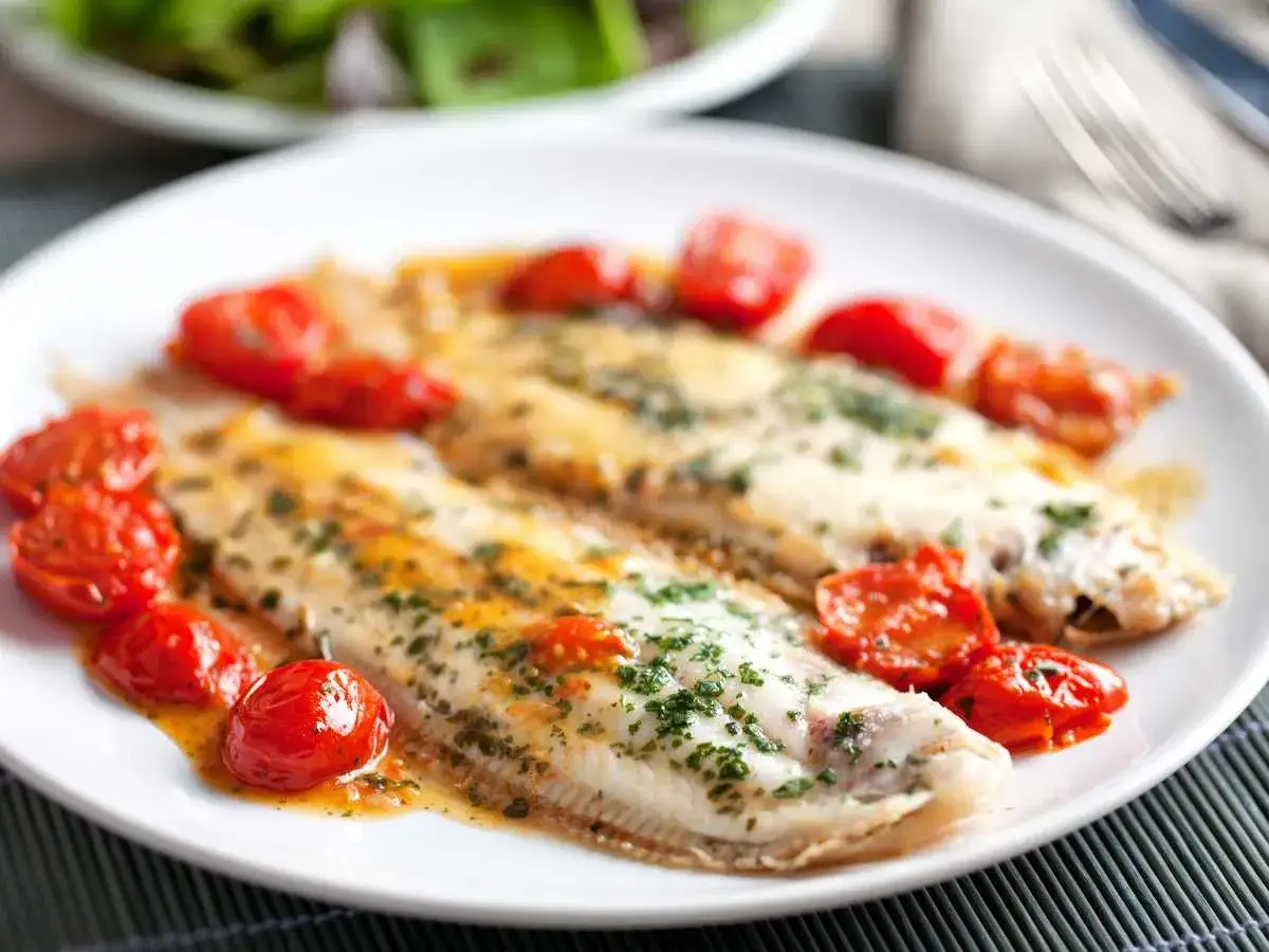 Dos filetes de lenguado a la plancha con tomates cherry salteados y perejil picado, servidos en un plato blanco.