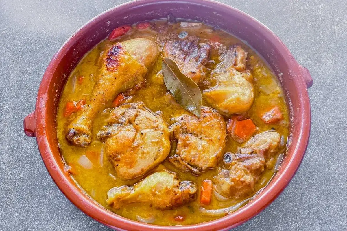Pollo en salsa de la abuela, jugoso y dorado, con trozos de zanahoria y cebolla en una cazuela de barro.
