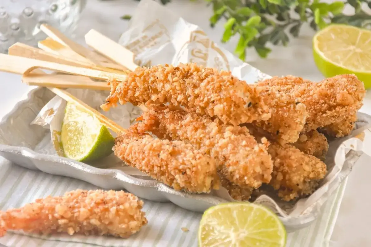Gambas a la gabardina crujientes en brochetas, servidas con gajos de lima.