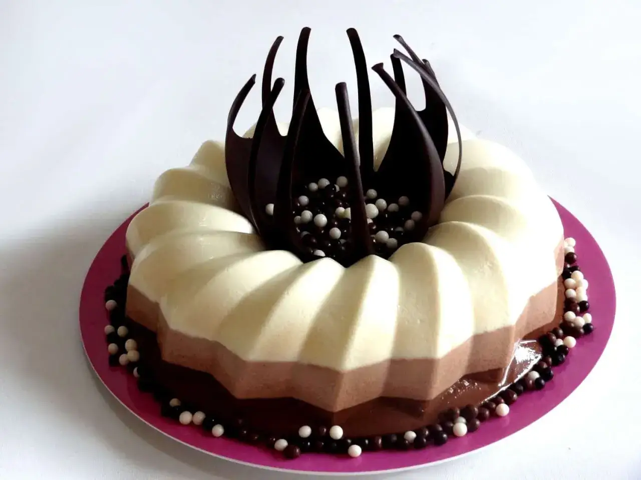 Deliciosa tarta de tres chocolates, con capas de blanco, con leche y negro, decorada con virutas de chocolate y bolitas.