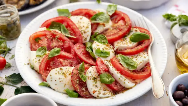 Ensalada caprese fresca con rodajas de tomate y mozzarella, aderezada con albahaca y especias.